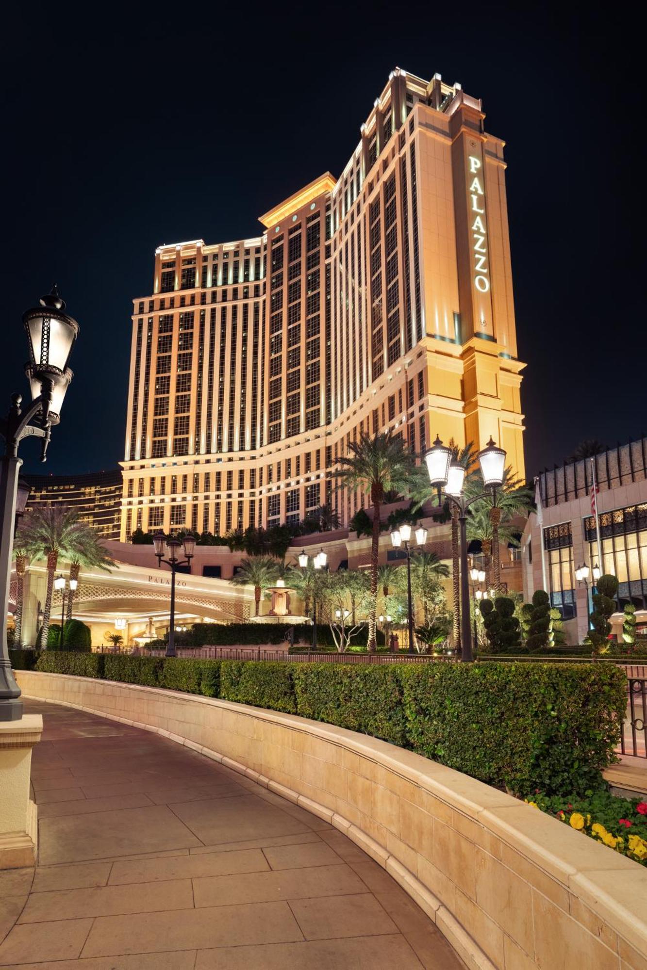 Hotel The Palazzo at The Venetian® Las Vegas Esterno foto The photo depicts a large, illuminated hotel building at night. The architecture is modern and elegant, featuring tall structures with decorative lighting. Surrounding the hotel are neatly trimmed hedges and palm trees, contributing to a luxurious at
