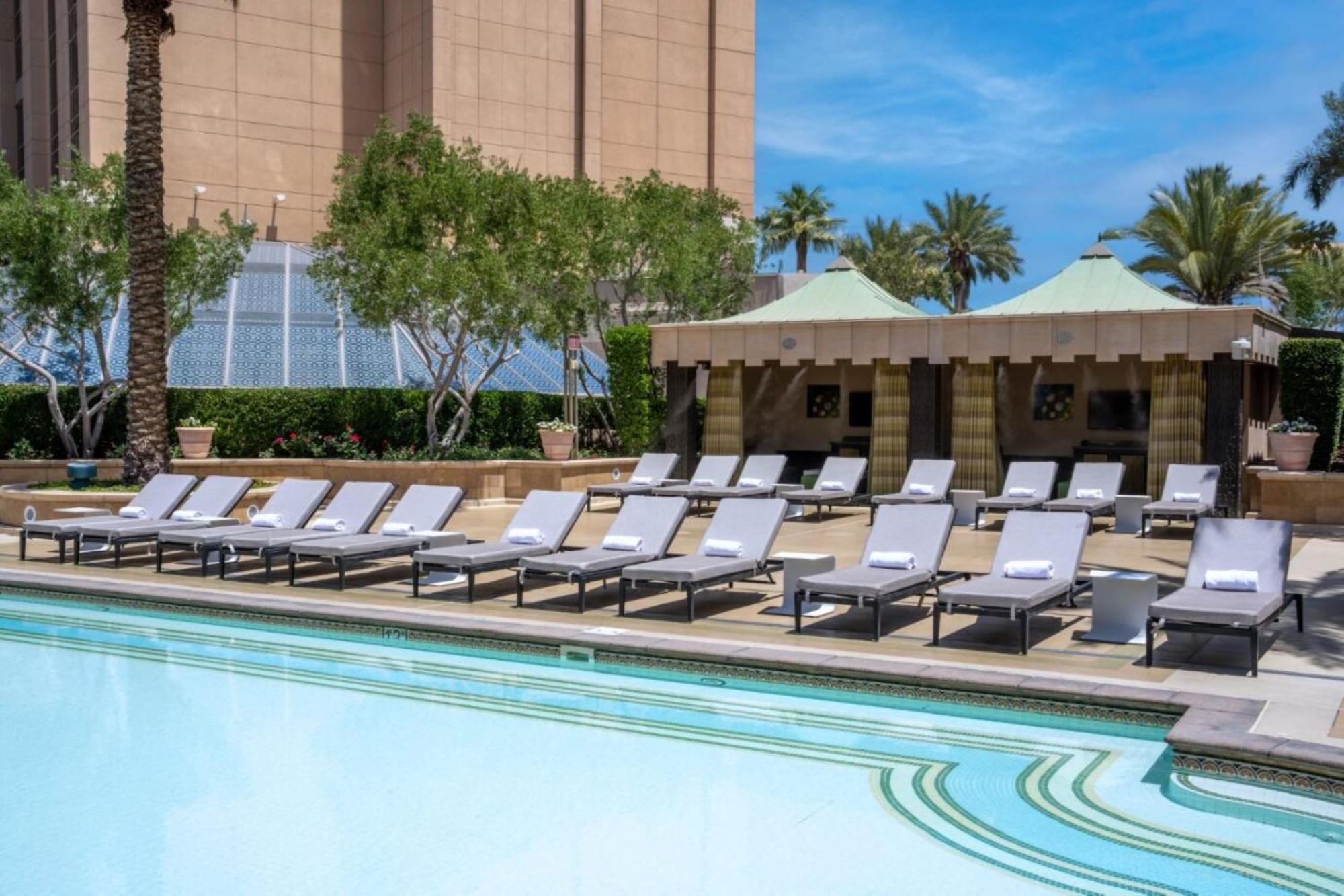 Hotel The Palazzo at The Venetian® Las Vegas Esterno foto The photo shows a tranquil outdoor pool area, featuring several modern lounge chairs arranged neatly by the water's edge. The pool has a clear blue surface, reflecting the sky. In the background, there are palm trees and some greenery, suggesting a t